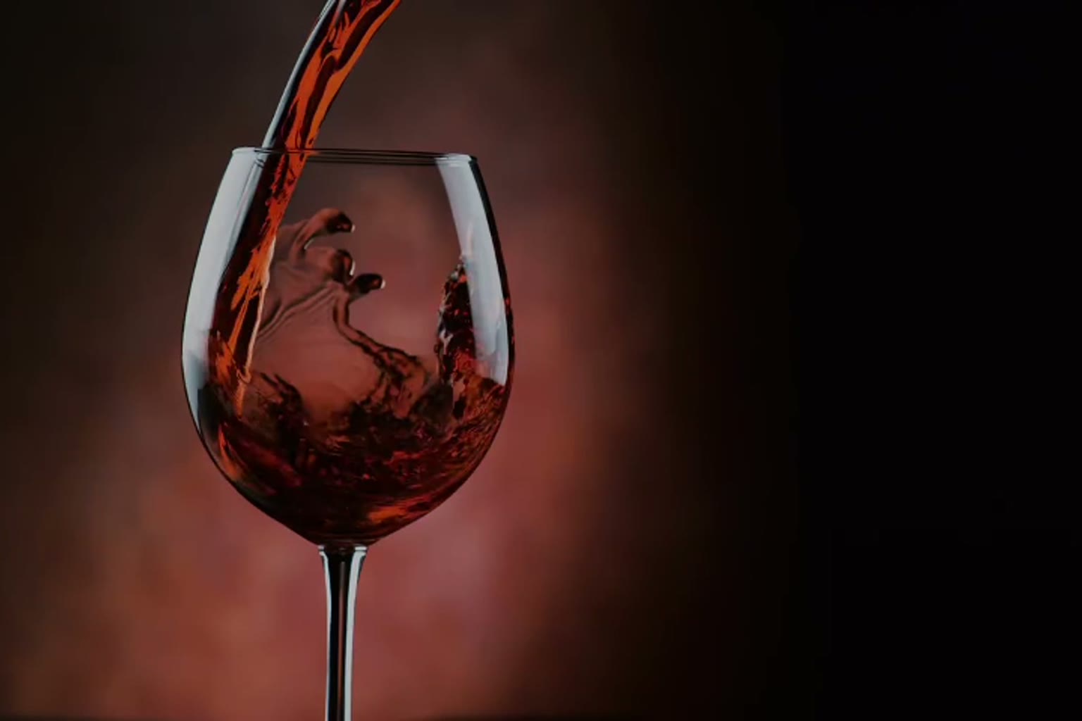 Red wine pouring into a glass in low warm light